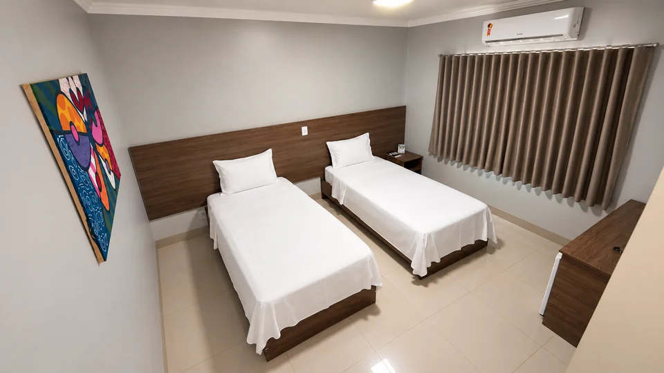 Suíte Duplo do Planalto Palace Hotel em Rurópolis, com duas camas de solteiro, ar-condicionado, cortinas e quadro colorido.